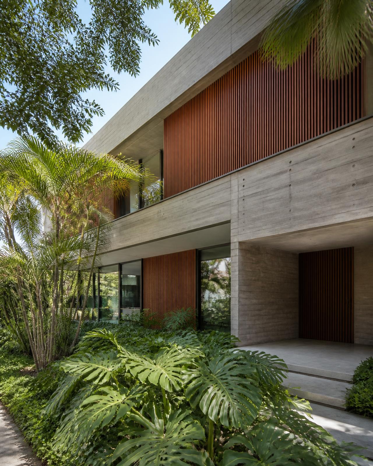 Fachada de residência contemporânea brasileira em concreto aparente e madeira, com paisagismo tropical